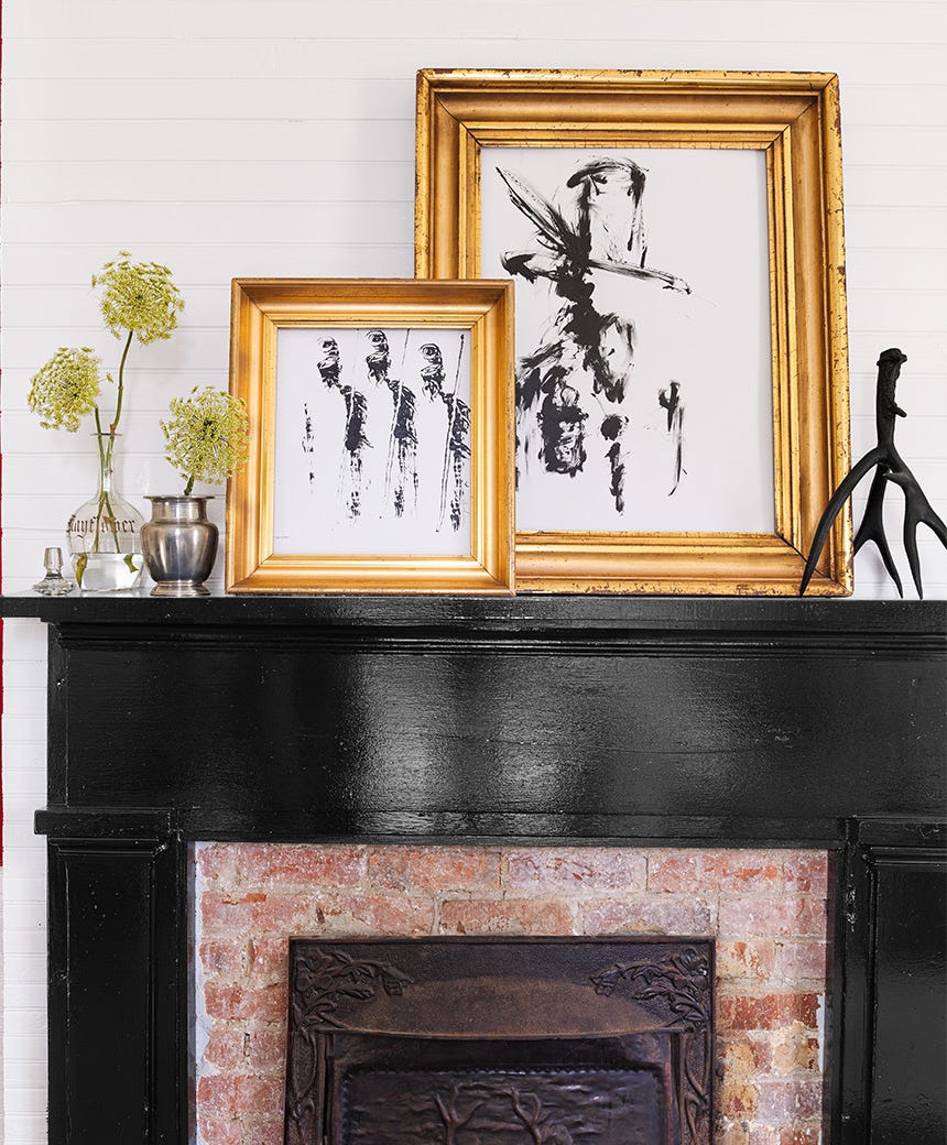 brick fireplace with glossy black painted wood surround, framed modern art and flowers in vintage vases decorate mantel