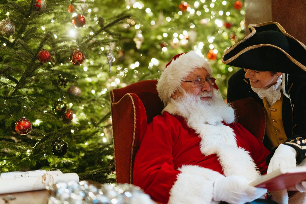 santa claus seated with a character in historical attire surrounded by a decorated christmas tree