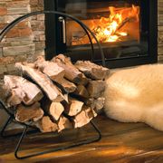 circular iron firewood rack in front of fireplace with sheepskin rug and pinecones