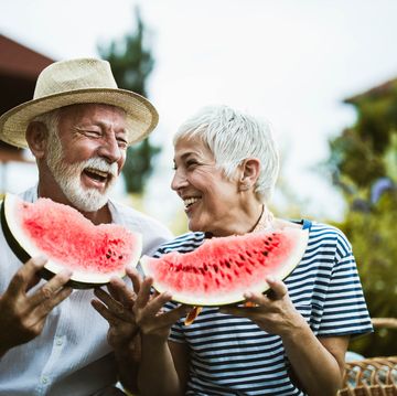 cheerful senior couple having fun while eating watermelon in the backyard