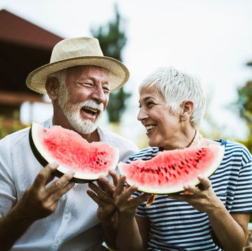 cheerful senior couple having fun while eating watermelon in the backyard