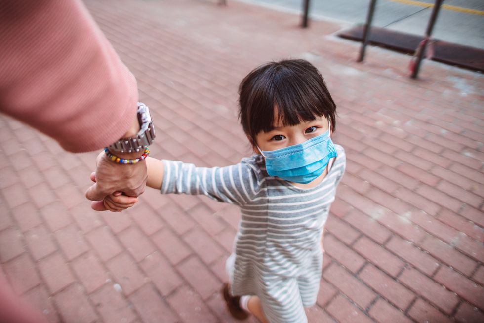 first person perspective of dad holding little daughter's hand who's wearing a medical face mask while they strolling on the street joyfully