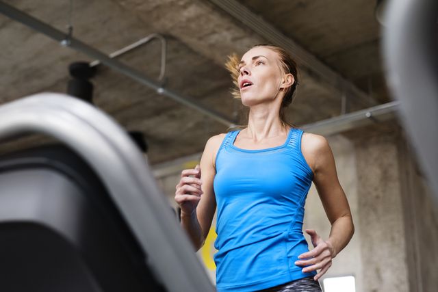 Fit attractive woman in blue tanglet running on treadmill in modern gym