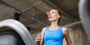 Fit attractive woman in blue tanglet running on treadmill in modern gym