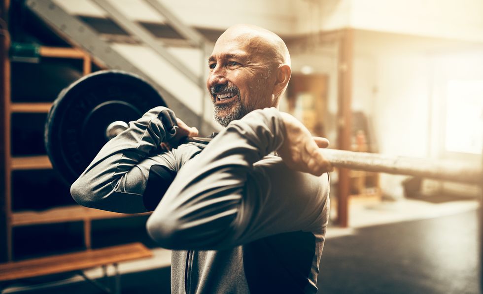 Fit mature man lifting weights and smiling in a gym