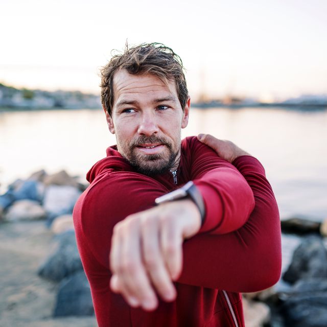 a fit mature sportsman runner doing exercise outdoors on beach, stretching.