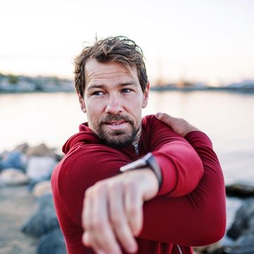 a fit mature sportsman runner doing exercise outdoors on beach, stretching.