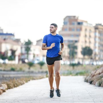 fit young man in sportswear running on road and warming up