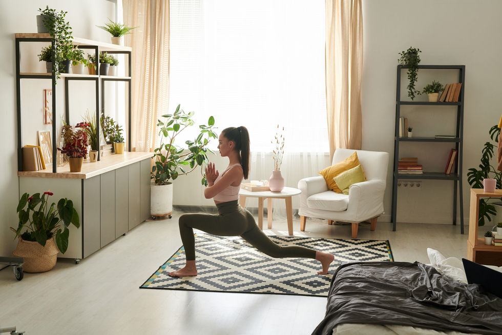 fit young woman with ponytail holding hands in namaste while doing warrior pose in living room
