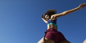young female athlete jumping against clear blue sky on sunny day