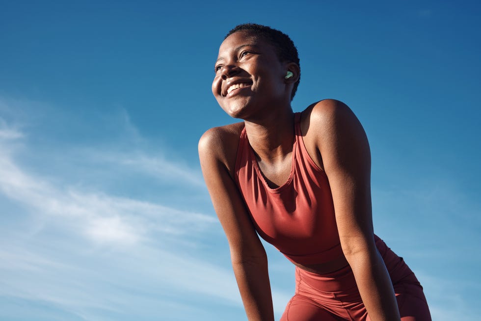 fitness, black woman and happy athlete smile after running, exercise and marathon training workout blue sky, summer sports and run of a african runner breathing with happiness from sport outdoor