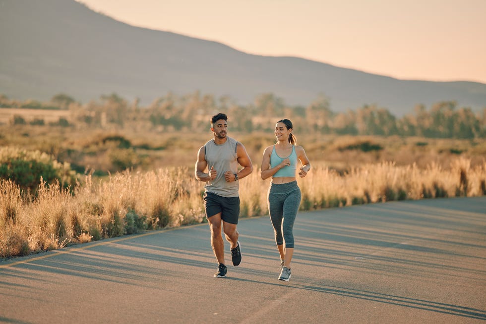 fitness, exercise and couple on road running together at sunset for wellness, health and cardio sports, workout and young man and woman exercising, run and practice for marathon training on mountain