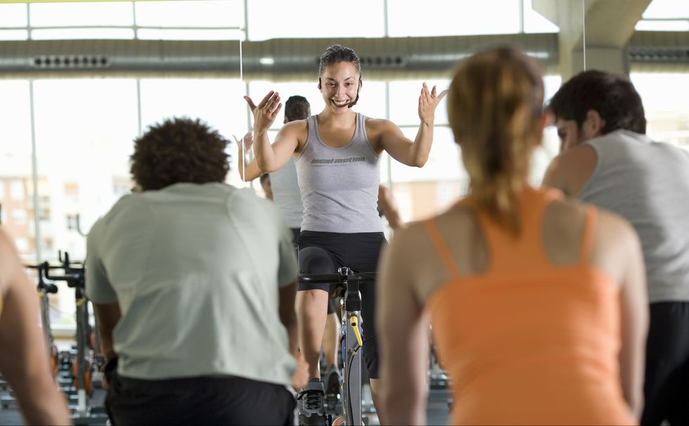 Fitness instructor leading class on exercise bicycles in gym, rear view