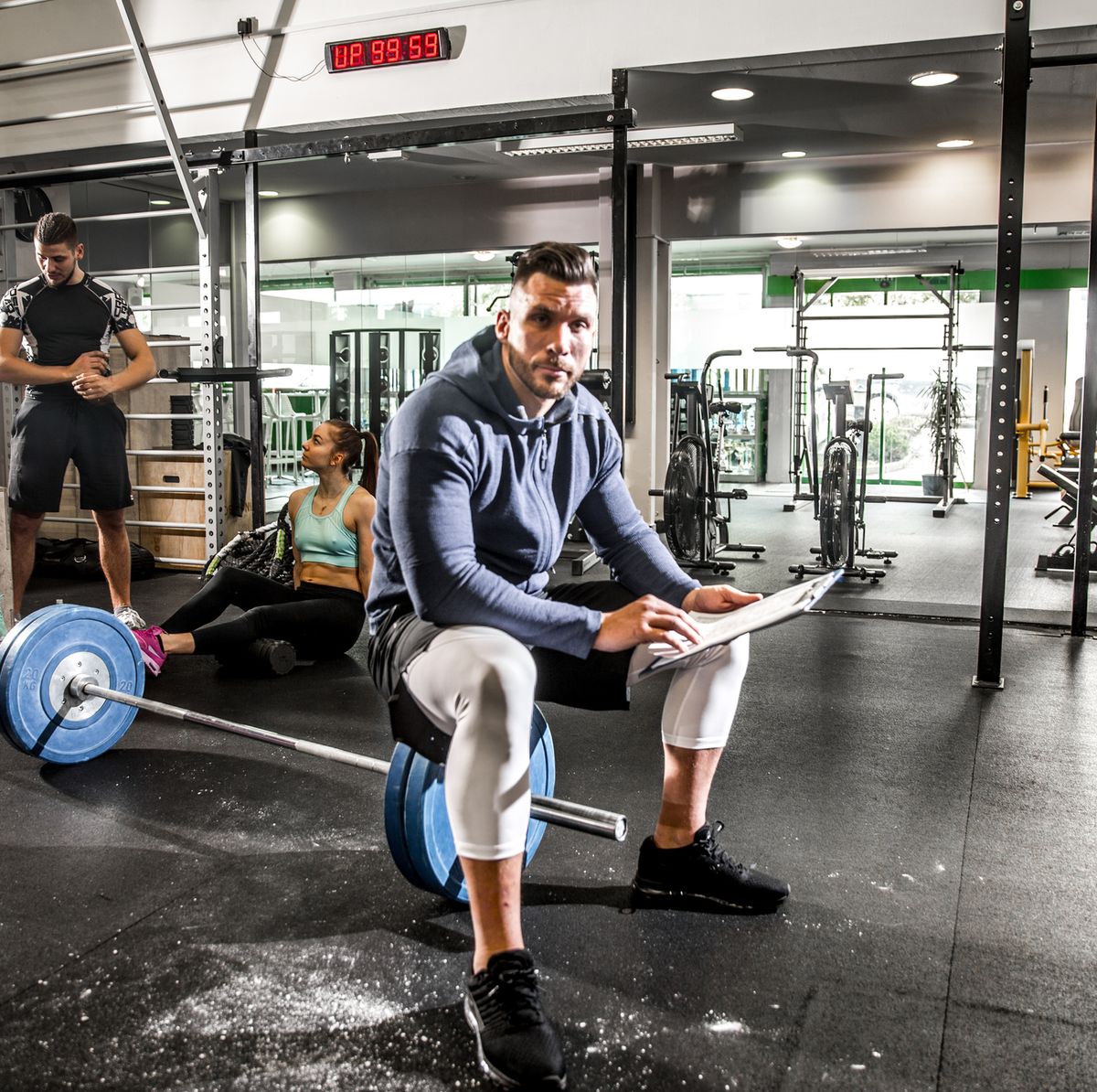 Fitness Instructor Sitting on Weights and Holding Written Training Program