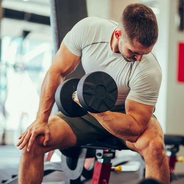 a fitness man is sitting in a gym and flexing muscles during his training with a dumbbell