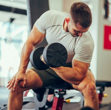 a fitness man is sitting in a gym and flexing muscles during his training with a dumbbell