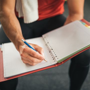fitness personal trainer writing on notebook sitting on gym bench