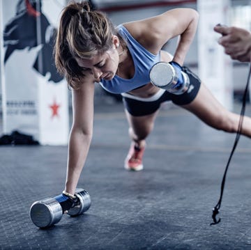 Fitness trainer keeping time with woman doing dumbell push-ups