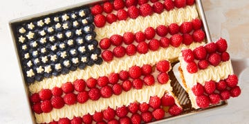 white cake decorated to look like an american flag with blueberries for stars, raspberries for red stripes, and off white frosting for white stripes