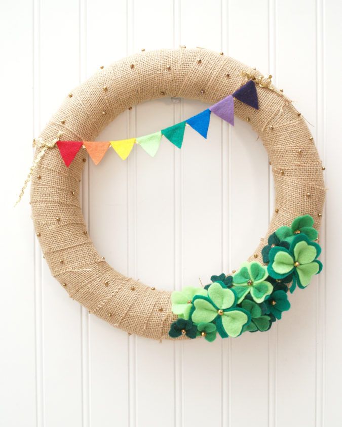 A wreath made of sparkly gold burlap with a green felt shamrock at the bottom and a small felt rainbow at the top.