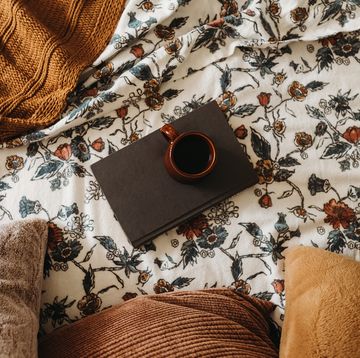 coffee and book on top of floral print flannel sheets