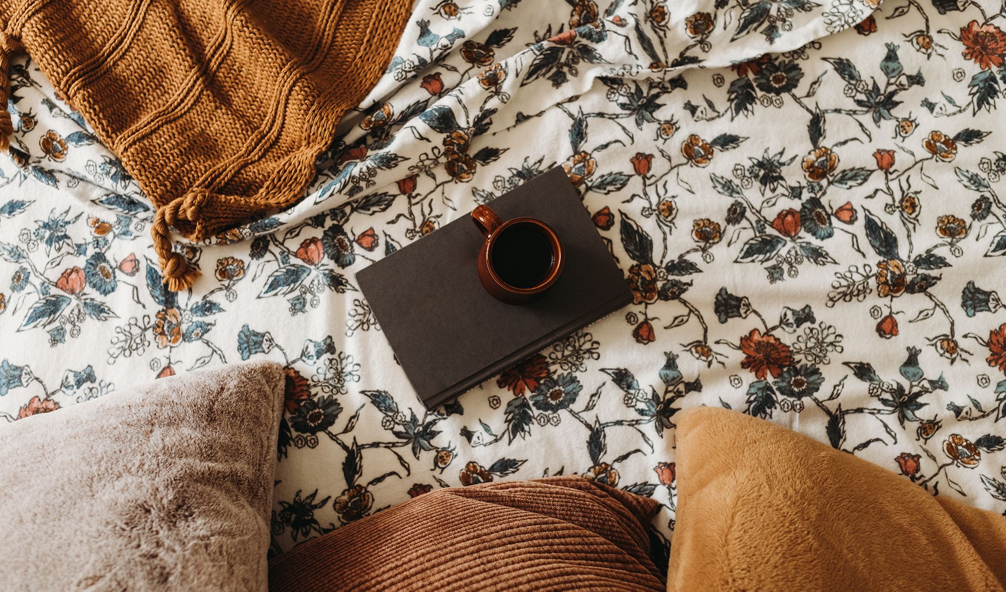 coffee and book on top of floral print flannel sheets
