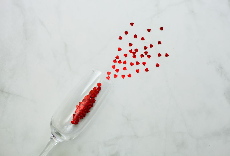 flat lay of champagne glass with red heart confetti over gray background greeting card for valentine's day