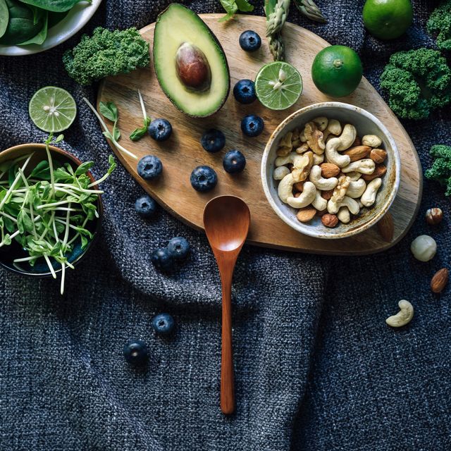 flat lay of fresh and healthy green fruits and vegetables with a bowl of mixed nuts on a rustic wooden board, against a dark grey fabric background for a healthy eating diet healthy superfood, green colour and detox diet concept