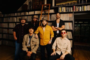 group of individuals posed in front of a bookshelf filled with vinyl records