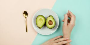 flatlay with cut avocado on white plate and woman's hands on pastel background, healthy diet concept