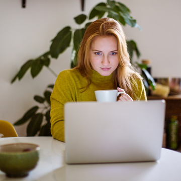 a woman works from home on her laptop drinking tea