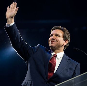 ron desantis waving to an audience with his right hand as he stands at a podium