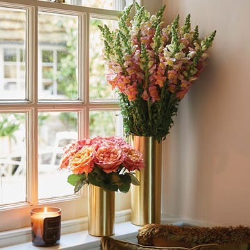 best flower subscriptions 2024 two flower arrangements in gold vases near a window next to a candle in a roundup of the best flower subscriptions 2024