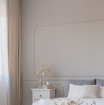 flowers in grey vase on the floor of simple bedroom with grey wall and white furniture, copy space on empty wall