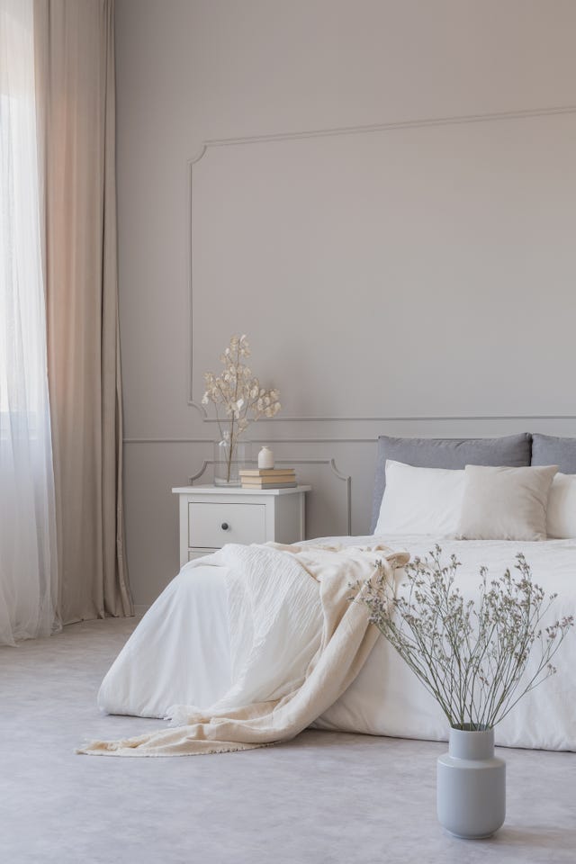 flowers in grey vase on the floor of simple bedroom with grey wall and white furniture, copy space on empty wall