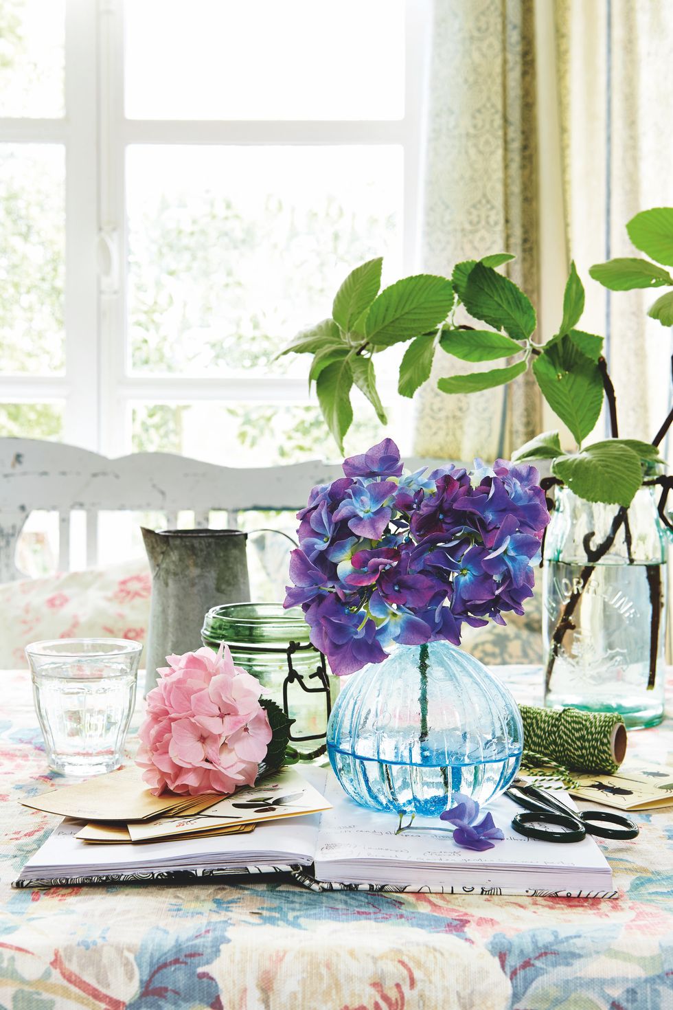blue and pink hydrangea flowers, blue glass vase, scrap book, branches wtih foliage, leaves, vases, floral pattern tablecloth, summer, flower arranging