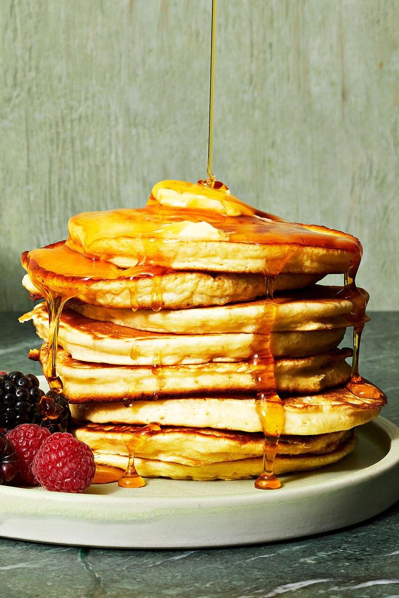 a stack of fluffy pancakes with syrup and mixed berries on the side