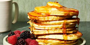 a stack of fluffy pancakes with syrup poured on top and berries on the side