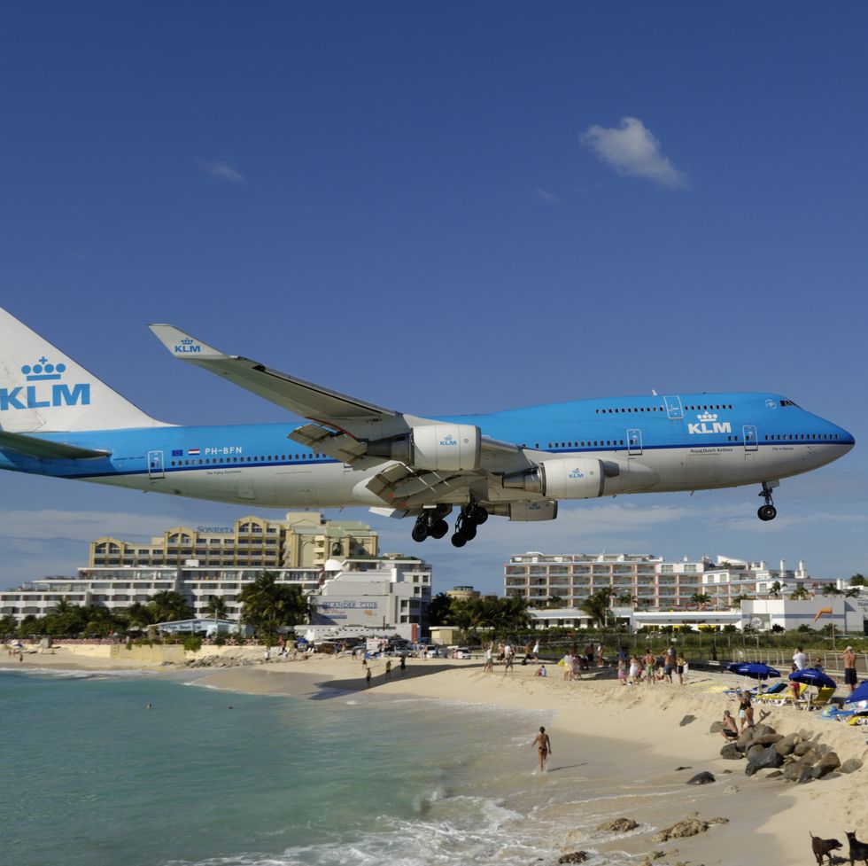 flying low on final approach landing over maho beach with hotels behind b747 on the runway with hills behind