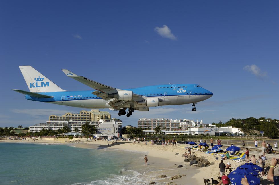 flying low on final approach landing over maho beach with hotels behind b747 on the runway with hills behind
