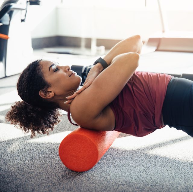 young woman stretching her back at the gym, using a foam roller