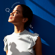 a woman standing against a blue wall with closed eyes looking toward the sun
