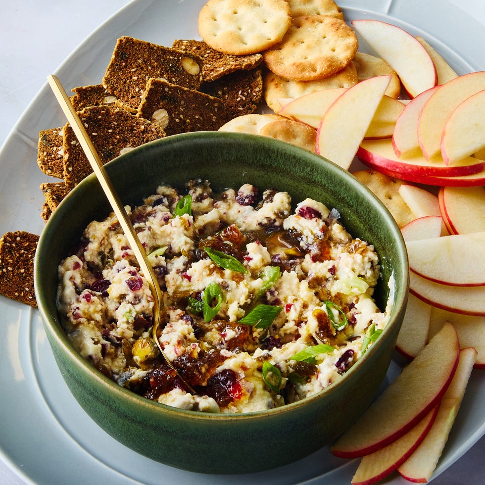 a green bowl filled with a creamy dip surrounded by crackers and apple slices