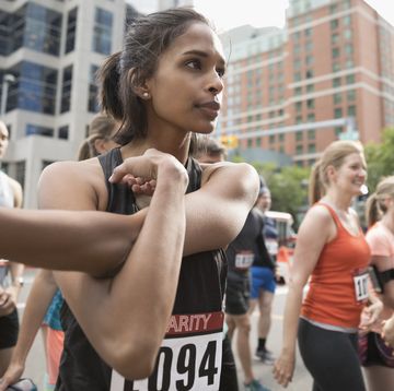 Focused female runner stretching arm on urban street