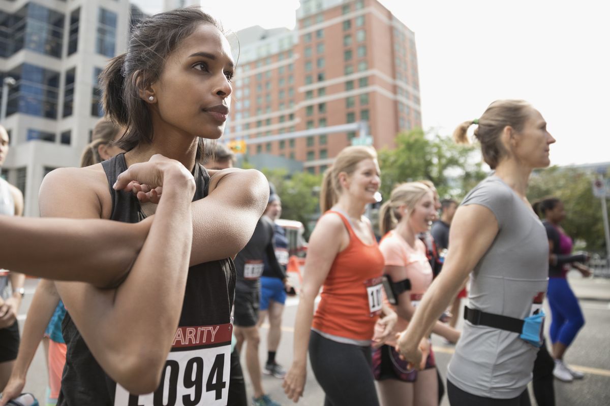 Focused female runner stretching arm on urban street
