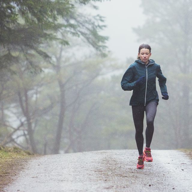focused woman jogging on trail in rainy woods