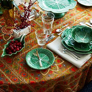 a table set with an orange and brown tablecloth cabbage ware and red accents