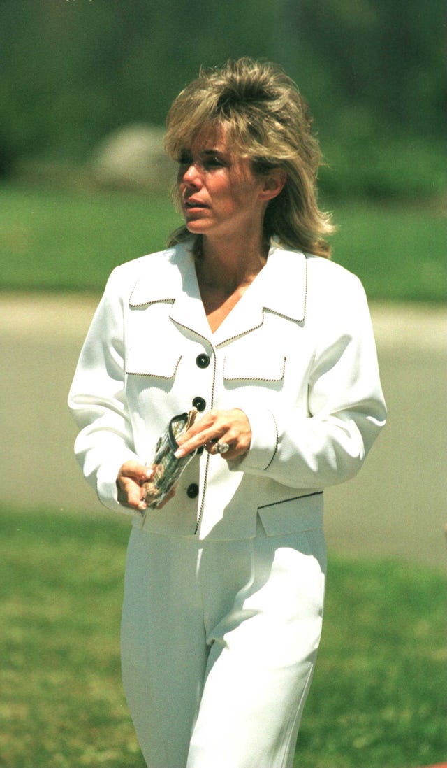 tammi saccoman walks outside and holds a clear satchel full of money, she wears an all white suit