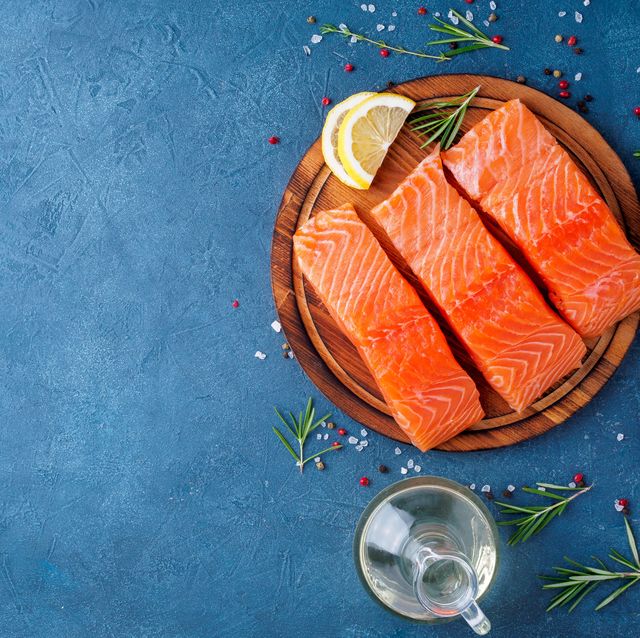 food background, sliced portions large salmon fillet steaks on chopping board on dark blue concrete table, copy space, top view