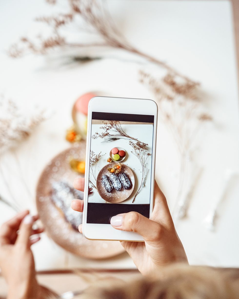 food blogger young woman sitting taking photo of desserts on plate on smartphone top view close up